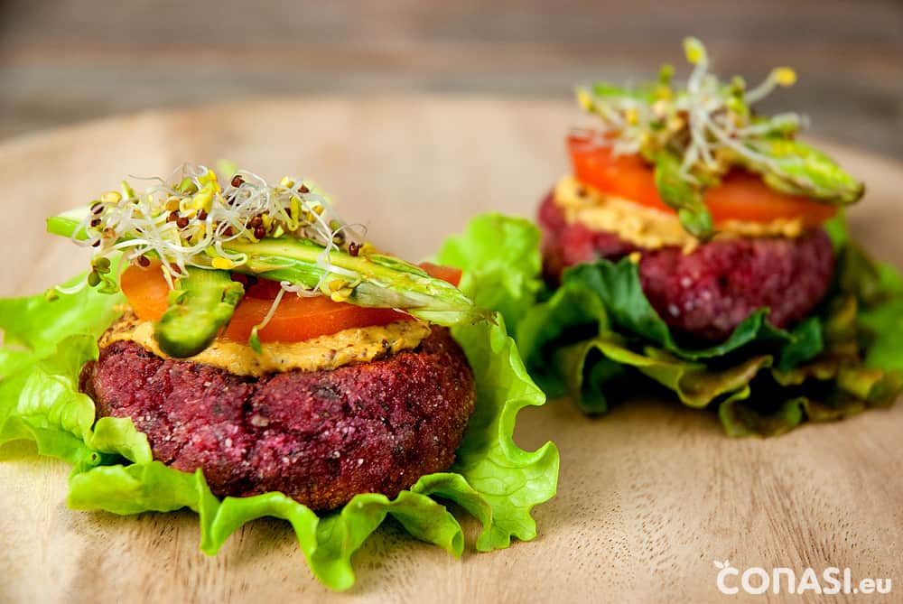 Hamburguesas veganas sobre hoja de lechuga, servidas con germinados y verduras.