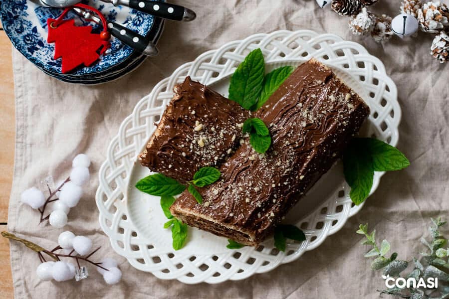 Tronco de Navidad sobre un plato decorado con hojas de hierbabuena